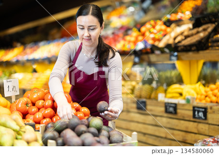 Female salesperson carefully places ripe passion fruit on the counter of grocery supermarket 134580060