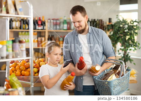 European man with son customer at shop scans QR code on juice bottle using phone camera 134580186