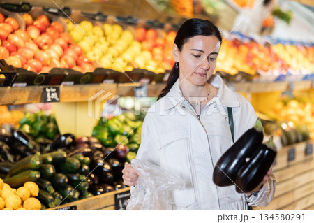 Female shopper carefully selecting ripe zucchini in supermarket Female shopper carefully selecting ripe zucchini in supermarket 134580291