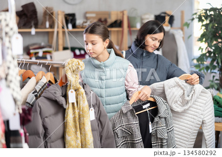 Teenage girl with her mother chooses coat or down jacket Teenage girl with her mother chooses coat or down jacket 134580292