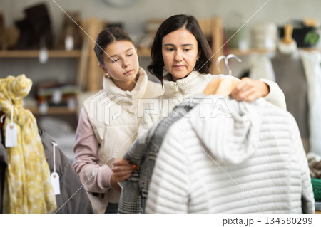 Mother and teen daughter looks at products in store and selects coat or jacket. 134580299