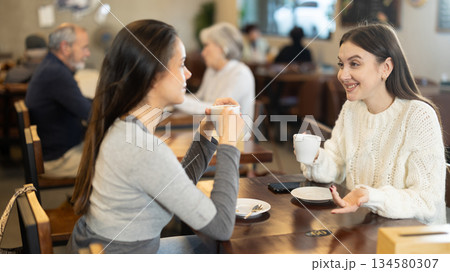 Two young women drinking coffee and talking in cafe Two young women drinking coffee and talking in cafe 134580307