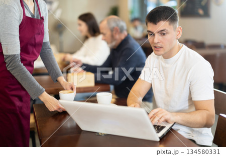 Young female waitress brings coffee to man with laptop 134580331
