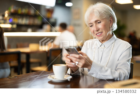 Elderly woman sitting with mobile phones in cafe Elderly woman sitting with mobile phones in cafe 134580332