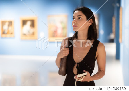 Woman with phone in hands in museum hall, view painting exhibition Woman with phone in hands in museum hall, view painting exhibition 134580380