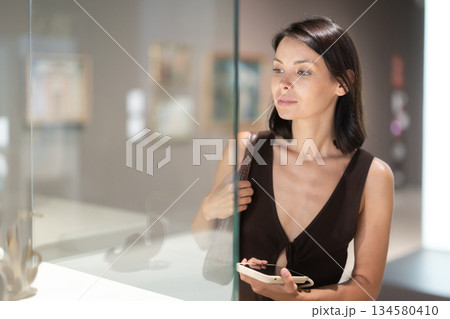 Young female visitor stands near glass display case in museum 134580410