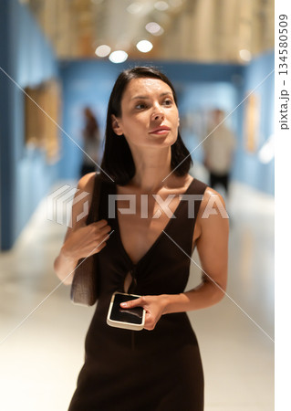 Woman with phone in hands in museum hall, view painting exhibition Woman with phone in hands in museum hall, view painting exhibition 134580509