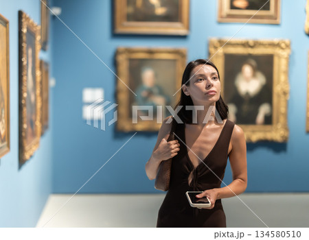 Woman visiting museum and looking at paintings in gold frames Woman visiting museum and looking at paintings in gold frames 134580510