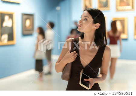 Woman visiting museum and looking at paintings in gold frames 134580511