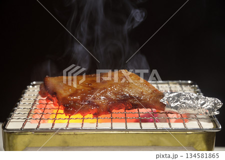 煙り立ち昇る七輪で鶏モモ肉を焼く 134581865