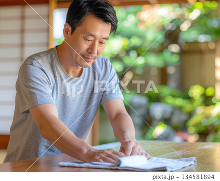 Man cleaning a wooden table with a cloth in a serene outdoor setting 134581894