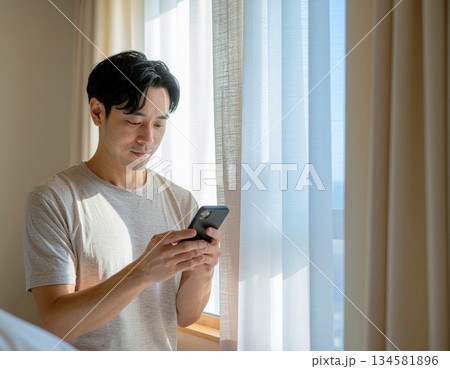 Young man engrossed in smartphone near window with natural light 134581896