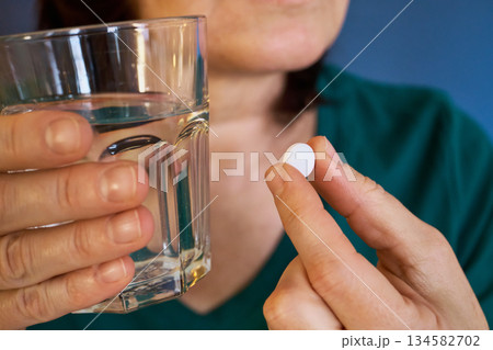 Woman holding white pill and glass of water, preparing medicine Woman holding white pill and glass of water, preparing medicine 134582702