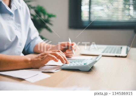 Office worker calculating expenses with a calculator while reviewing receipts and financial documents, representing accounting tasks, budgeting, money management and professional financial workflow. Office worker calculating expenses with a calculator while reviewing receipts and financial documents, representing accounting tasks, budgeting, money management and professional financial workflow. 134586915
