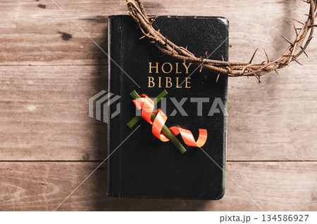 Crown of thorns with wooden cross, iron nail, ribbon on Bible, symbolizing Christian faith, sacrifice, crucifixion, Easter reflection, religious background for worship, prayer, devotion concepts Crown of thorns with wooden cross, iron nail, ribbon on Bible, symbolizing Christian faith, sacrifice, crucifixion, Easter reflection, religious background for worship, prayer, devotion concepts 134586927