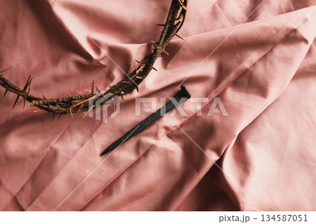 Crown of thorns, iron nail on soft pink fabric, symbolizing Christian faith, sacrifice, crucifixion, Easter reflection, religious background, worship, prayer, spiritual devotion concepts Crown of thorns, iron nail on soft pink fabric, symbolizing Christian faith, sacrifice, crucifixion, Easter reflection, religious background, worship, prayer, spiritual devotion concepts 134587051
