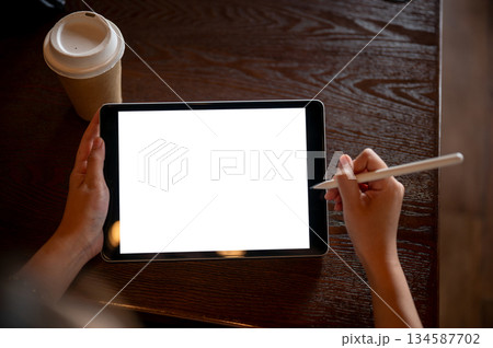 Top view close up of a hand holding a stylus pen over a white screen tablet placing on wooden table. 134587702