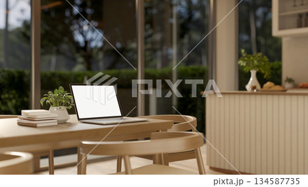 Blank screen laptop and books on wooden table with armchairs in cafe or coffee house with glass wall 134587735