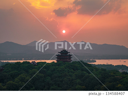 Aerial view of Chenghuang pagoda at sunset over Xihu lake in Hangzhou featuring mountains and lush green trees 134588407
