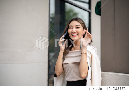 Long hair asian woman talking on phone while standing near the building pillar and raising her hand Long hair asian woman talking on phone while standing near the building pillar and raising her hand 134588572