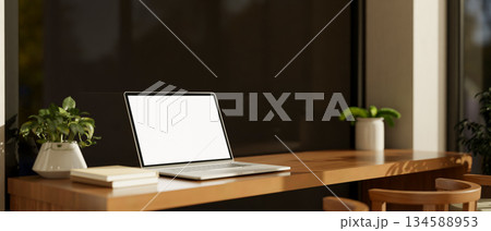 Blank screen laptop and books on a wooden table next to tinted glass wall in a cafe or coffee house. 134588953