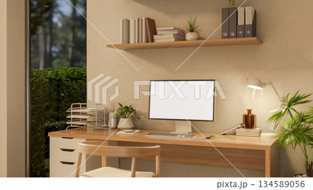 Blank screen computer on wooden desk under hanging display shelf and a chair in a cosy study room. 134589056