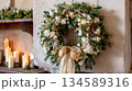 Elegant Christmas wreath adorned with white flowers and golden ribbon on rustic wall 134589316