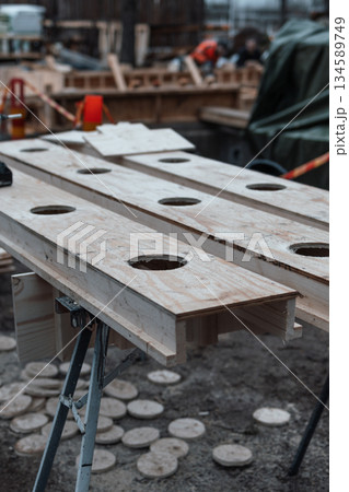 Wooden workbench with circular cutouts, surrounded by construction materials and tools, showcasing craftsmanship and industrial workspace atmosphere in a busy workshop environment Wooden workbench with circular cutouts, surrounded by construction materials and tools, showcasing craftsmanship and industrial workspace atmosphere in a busy workshop environment 134589749