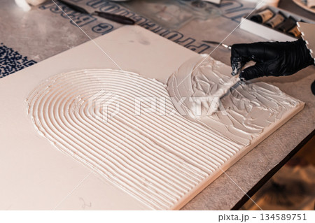 Artist applying textured white paste on canvas with a spatula, creating a unique abstract design, showcasing creativity and craftsmanship in modern art 134589751