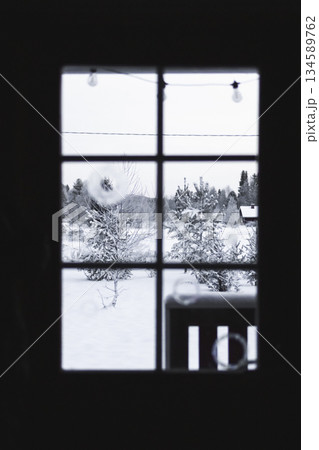 Winter landscape viewed through a window, showcasing snow-covered trees and a serene outdoor scene, with soft lighting creating a cozy atmosphere and inviting ambiance 134589762