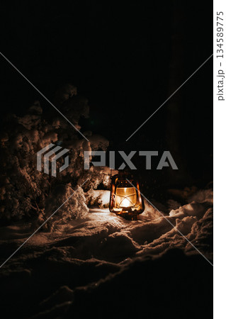 Vintage lantern illuminating snowy landscape at night, surrounded by soft snow-covered ground and dark trees, creating a warm and inviting atmosphere in a winter scene Vintage lantern illuminating snowy landscape at night, surrounded by soft snow-covered ground and dark trees, creating a warm and inviting atmosphere in a winter scene 134589775