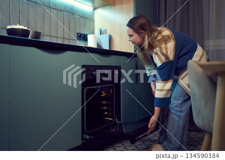 Focused woman checking meal in oven during mindful cooking routine Focused woman checking meal in oven during mindful cooking routine 134590384