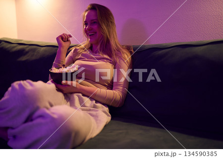 Female enjoying popcorn while watching screen on sofa at home 134590385