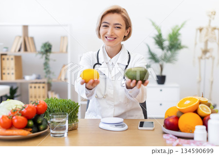 A smiling nutritionist holds a lemon and an avocado, promoting healthy eating and diet. A smiling nutritionist holds a lemon and an avocado, promoting healthy eating and diet. 134590699