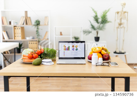 A laptop displays a healthy diet plan, surrounded by fresh fruits, vegetables, and supplements on a wooden table. A laptop displays a healthy diet plan, surrounded by fresh fruits, vegetables, and supplements on a wooden table. 134590736