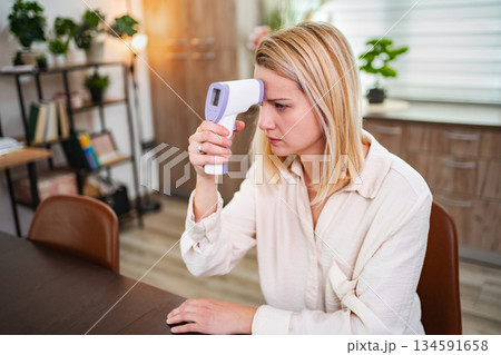 Woman checks her temperature with a digital thermometer at home Woman checks her temperature with a digital thermometer at home 134591658