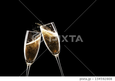 Two champagne flutes clinking in a festive toast. Golden bubbles and splashes against a dramatic black background. Elegant celebration, New Year, or wedding concept with copy space. 134592808