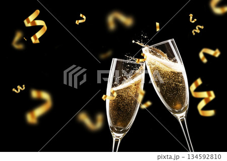 Two champagne flutes clinking with golden confetti falling on a black background. Festive toast, luxury celebration, New Year party, and wedding anniversary concept with elegant splashes. Two champagne flutes clinking with golden confetti falling on a black background. Festive toast, luxury celebration, New Year party, and wedding anniversary concept with elegant splashes. 134592810