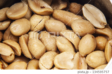 Macro shot of a scattering of roasted peanut halves with salt. The dense texture of these popular nuts, the concept of a healthy snack, protein, and natural food. Macro shot of a scattering of roasted peanut halves with salt. The dense texture of these popular nuts, the concept of a healthy snack, protein, and natural food. 134595757