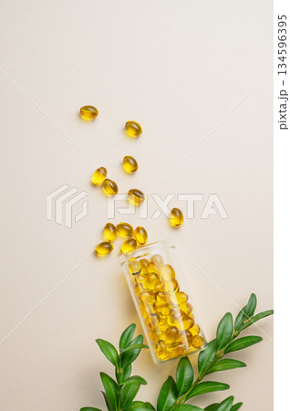 Yellow softgel vitamins capsules scattered in a bottle on a light background with green leaf. 134596395