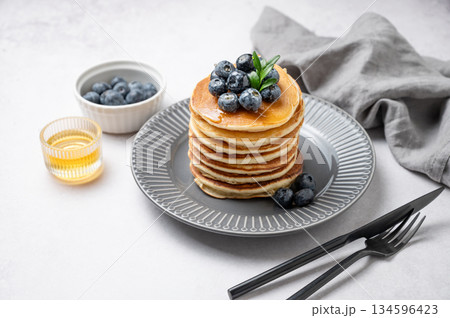 Stack of pancakes with fresh blueberries and suryp on a gray plate on a light background 134596423