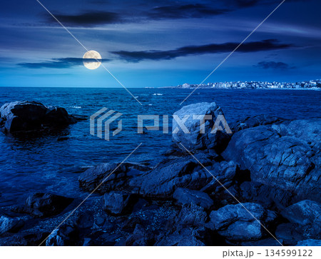 rocky shore of the sea coast under blue sky at night. beautiful view of coastal scene in full moon light. resort scenery during vacation season in summer. backdrop for fiction art or mystery concepts rocky shore of the sea coast under blue sky at night. beautiful view of coastal scene in full moon light. resort scenery during vacation season in summer. backdrop for fiction art or mystery concepts 134599122