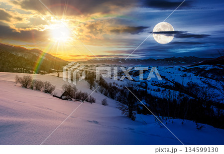 winter in mountainous countryside. day and night time change concept. gorgeous cloudy sky over the snow covered hills with sun and moon at twilight. wide mountain ridge in a far distance. equality and 134599130
