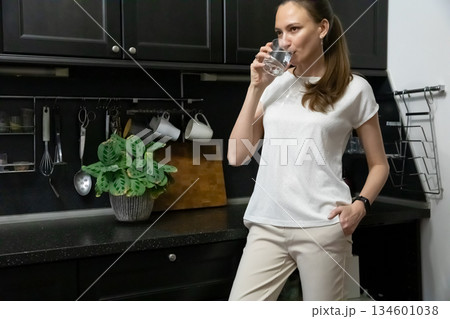 Young Woman Drinking Water in Modern Kitchen Setting 134601038