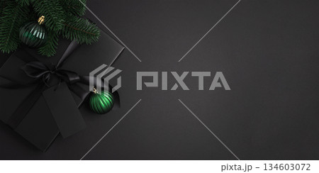 Black Christmas Gift Box with Satin Ribbon and Green Ornaments on Dark Holiday Background Black Christmas Gift Box with Satin Ribbon and Green Ornaments on Dark Holiday Background 134603072