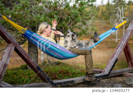Woman relaxing in hammock with dog wearing outdoor clothing in forest nature Woman relaxing in hammock with dog wearing outdoor clothing in forest nature 134603277