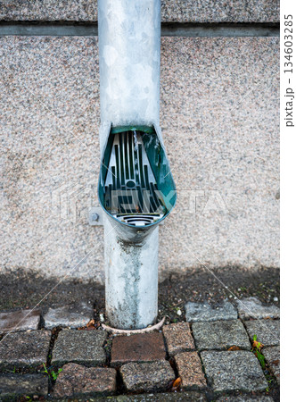 Rainwater downspout with drain grate on stone pavement 134603285