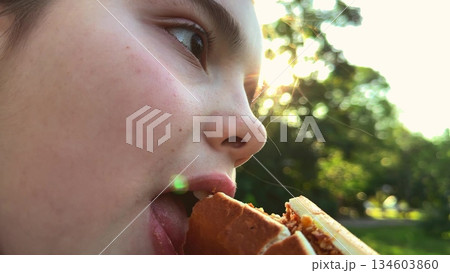 Sunset snacking, leafy background, content child, big sandwich, striped fashion, eating outside, glowing sun, nature all around, relaxed mood, yummy meal, Childhood joy, green park scene, burger 134603860