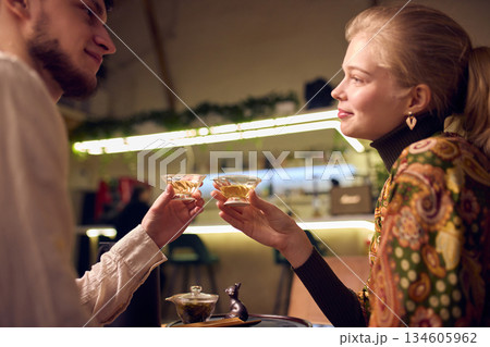 Young couple sharing tea and making toast with glass cups indoors Young couple sharing tea and making toast with glass cups indoors 134605962
