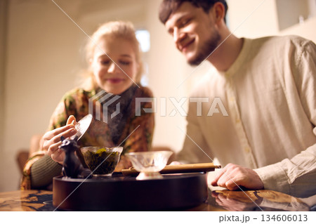 Woman lifting tea lid while observing brewing process 134606013